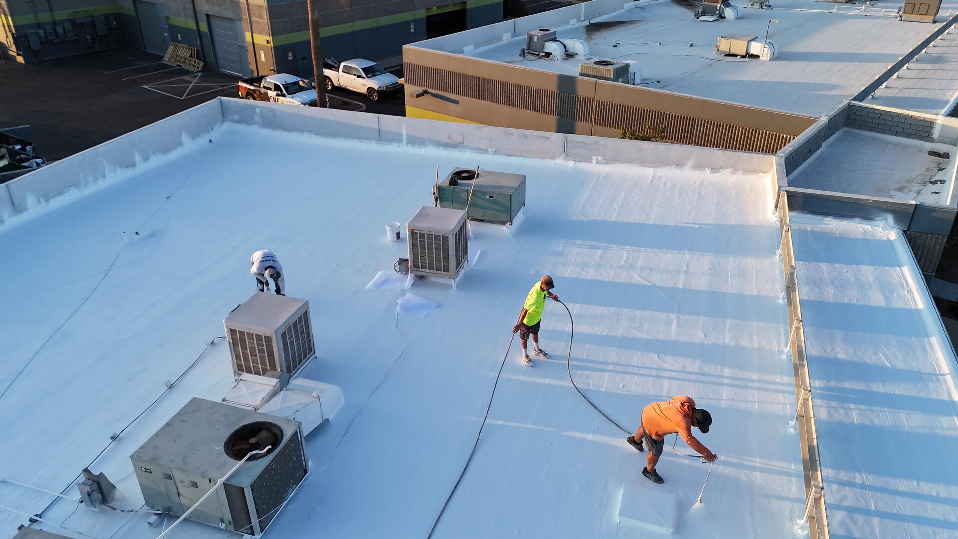 Aerial view of an FNF Roofing crew applying an acrylic roof coating to a commercial flat roof